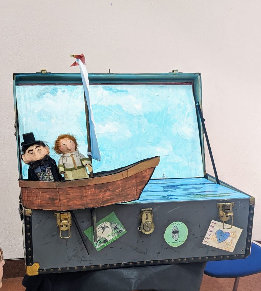 the puppets of the boat and the person from before with the person in the boat with another person in a top hat and a beard in a luggage container decorated to look like the sea